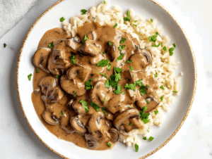 this image shows A creamy cornstarch and plant-based milk mixture being poured into the skillet with mushrooms, onions, and garlic, thickening into a luscious stroganoff sauce.