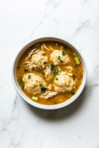 This image shows a bowl of homemade Chicken and Dumplings, filled with tender shredded chicken, soft dumplings, and a creamy, seasoned broth.
