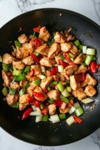 This image shows the signature Kung Pao sauce being poured into the wok, thickening into a glossy coating that clings to the chicken.