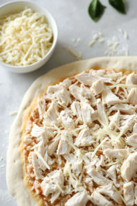 This image shows tender, cooked chicken pieces being placed on top of the cheese layer, creating a hearty and flavorful filling for the Chicken Alfredo Calzones.