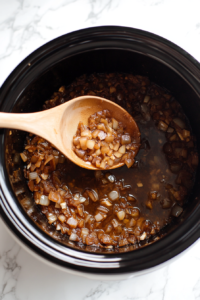 This image shows the cooked onion and garlic mixture being carefully transferred into the slow cooker, forming the base of the flavorful chicken and rice dish.