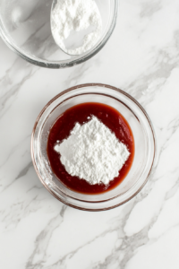 This image shows ketchup and cornstarch being stirred into the sauce, thickening it into a glossy, flavorful sweet and sour mixture.