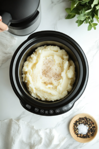 This image shows a hand sprinkling seasonings, such as salt and pepper, into the mashed potatoes for added taste.