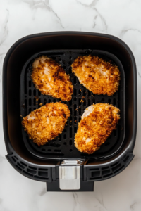 This image shows breaded Chicken Kiev cooking in an air fryer, turning golden brown with a perfectly crispy crust while locking in the flavorful butter filling.
