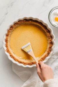 This image shows a pastry brush applying an egg wash to a pie crust, ensuring a golden and glossy finish when baked.