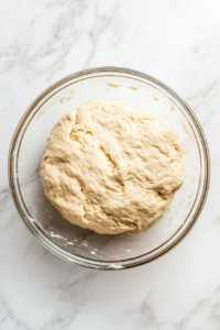 This image shows a bowl of babka dough covered with a cloth, allowing it to rise until doubled in size for a fluffy and soft texture.