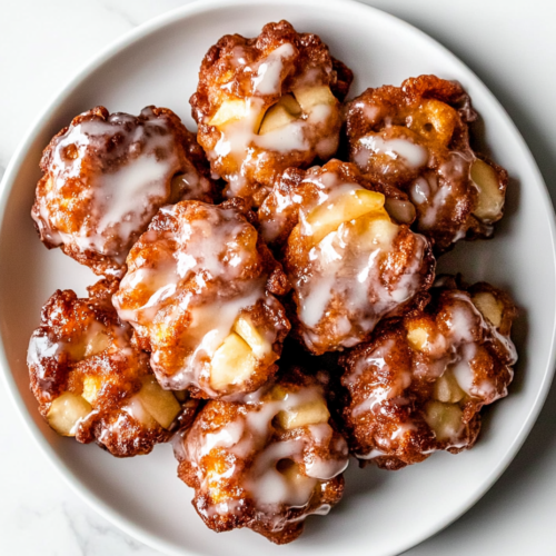 A plate of golden-brown baked apple fritters, perfectly glazed to harden, served on a clean white plate.