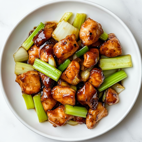 This image shows a plate of Black Pepper Chicken Panda Express, featuring glazed chicken pieces, celery stalks, and onions, served on a white round plate.