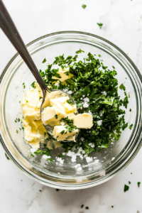 This image shows a bowl of softened butter being mixed with fresh herbs, garlic, and seasonings to create a rich and flavorful filling for Chicken Kiev.
