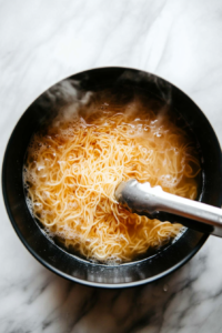 This image shows spaghetti noodles cooking in a pot of boiling water, softening to the perfect texture for stir-frying.
