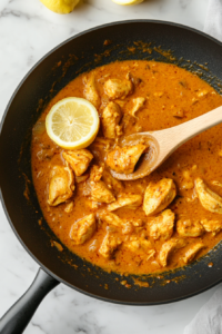This image shows fresh lemon juice and a sprinkle of cayenne pepper being stirred into the simmering curry, enhancing its zesty and spicy depth.