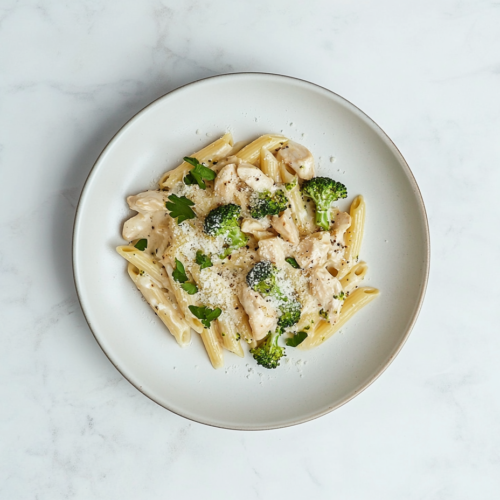 This image shows a delicious plate of Broccoli Chicken Penne Pasta served on a white round plate, garnished with grated cheese, chopped cilantro, and fresh broccoli pieces for a flavorful and comforting meal.