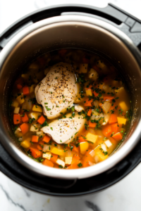 This image shows rich, flavorful broth being poured over the chicken, wild rice, and vegetables, preparing the dish for pressure cooking.