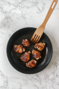 This image shows chicken thighs being seared skin-side down in a hot pan, creating a golden, crispy texture before they are added to the slow cooker.