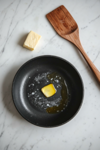 This image shows butter and olive oil melting in a hot skillet, creating a flavorful base for cooking the seasoned chicken.