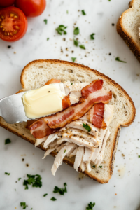 This image shows slices of bread being buttered and layered with turkey, cheese, and vegetables, preparing them to be cooked into a crispy turkey melt sandwich.