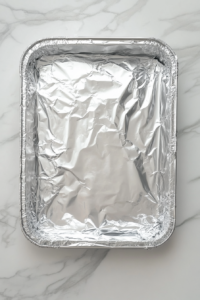 This image shows the assembled casserole being covered and placed in the oven to bake until creamy and tender.