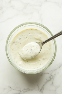 This image shows a spoon lifting freshly mixed Wingstop-style ranch dressing, demonstrating its creamy consistency and smooth texture.