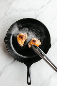 This image shows a top-down view of marinated chicken sizzling on a griddle pan, developing a golden-brown and flavorful crust.