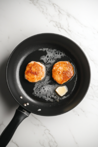 This image shows chicken pieces sizzling in a skillet, developing a golden-brown crust as they cook.