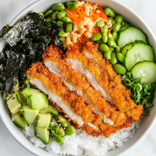 This image shows a beautifully arranged chicken katsu rice bowl with a base of fluffy rice, topped with crispy chicken katsu, fresh cucumber, avocado slices, pickled ginger, green onions, and nori, served in a white bowl.