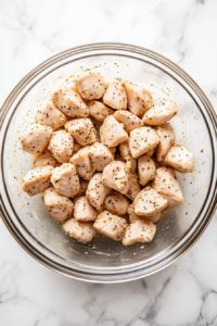 This image shows bite-sized pieces of chicken being evenly coated with a blend of ranch seasoning and spices for a bold, savory taste.