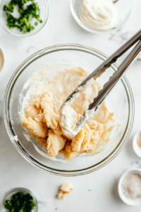This image shows a top-down view of raw chicken tenders being coated in a rich, seasoned mayo mixture for added flavor and moisture.