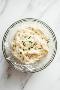This image shows a bowl of the prepared chicken fritter mixture covered with plastic wrap, allowing it to rest in the fridge for enhanced flavor and texture.