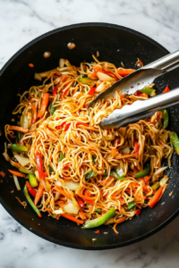 This image captures the moment when noodles and vegetables are tossed together in a pan for even coating with sauce.