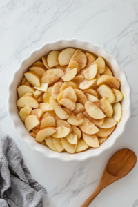 cinnamon-coated-apple-slices-being-transferred-to-a-baking-dish-for-apple-crisp