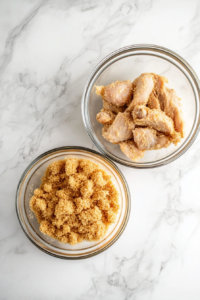 This image shows a chicken breast being dredged in crushed croutons, creating a crispy coating for a flavorful and crunchy texture when cooked.