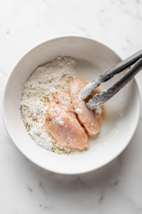 This image shows raw chicken pieces being coated in a mixture of seasonings and flour, preparing them for cooking in the garlic butter sauce.