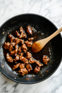 This image shows tender pieces of meat in a pan, coated in a flavorful sauce, sizzling and caramelizing to enhance their rich, deep flavor for Vietnamese rice bowls.