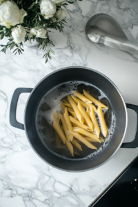 This image shows penne pasta being boiled in a large pot of water, cooking until tender and ready to be combined with chicken and broccoli.