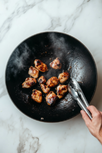 This image shows marinated chicken pieces sizzling in hot oil in a skillet, getting browned and crispy for the Black Pepper Chicken stir-fry.