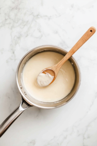This image shows a saucepan with glaze being stirred over heat until thickened to a silky consistency.