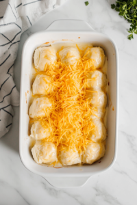 This image shows the rich sauce being poured over the stuffed crescent rolls, followed by a generous sprinkle of shredded cheese for extra indulgence.