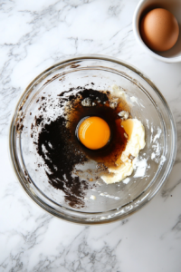 This image shows eggs and vanilla extract being added to the creamed butter and sugar mixture, enhancing the cookie dough with richness and flavor.
