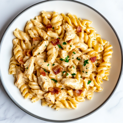 This image shows a plate of spiral rotini pasta coated in a rich, creamy ranch sauce, topped with crispy bacon bits and fresh cilantro garnish.