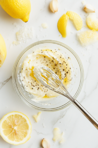 This image shows a smooth and creamy garlic aioli being whisked together, creating a flavorful dip that complements the crispy chicken fritters.