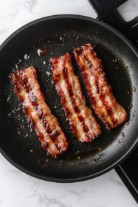 This image shows bacon sizzling in a hot pan, turning crispy and golden brown, ready to be added to the turkey melt sandwich for extra flavor.