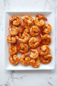This image shows golden-brown fried shrimp being arranged on a plate, ready to be coated in sauce and topped with walnuts.