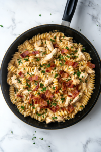 This image shows crispy bacon bits being sprinkled over the creamy pasta, adding a savory, smoky crunch to the dish.