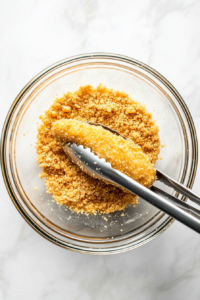 This image shows a top-down view of a bowl filled with finely crushed Ritz crackers, ready to be used as a crispy coating for the chicken tenders.