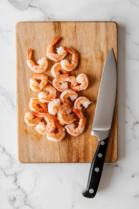 This image shows cooked shrimp being finely chopped on a cutting board, making them the perfect bite-sized pieces for the flavorful salsa.