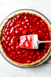 This image shows a spatula spreading a thick layer of glaze inside the baked pie crust, creating a rich and flavorful base.