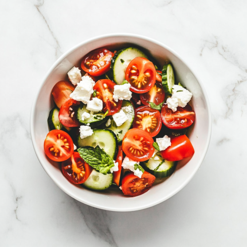 This image shows a vibrant bowl of tomato cucumber feta salad, featuring halved cherry tomatoes, round cucumber slices, and crumbled feta cheese on top for a refreshing and flavorful dish.