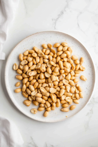 This image shows roasted peanuts spread on a plate to cool, ensuring they stay crisp and ready to be added to the final dish.