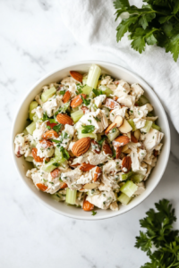This image shows a serving of Chicken Salad in a white bowl, garnished with extra almonds and celery, ready to be enjoyed as a light and refreshing meal