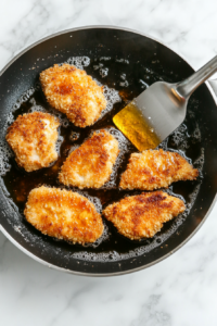 This image shows breaded chicken frying in hot oil, turning golden brown and crispy for the ultimate katsu texture.